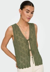 Zielona kamizelka dzianinowa z zapięciem na wstążkę, z teksturowanym wzorem i falbaniastym dołem. Bez rękawów, wykonana z lekkiego materiału.
