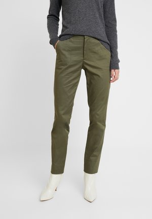 Olijfgroene slim-fit broek van een gladde stof met zijzakken, gecombineerd met puntige witte enkellaarsjes. Getextureerde grijze trui.