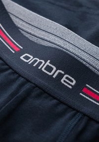 Marinblå elastisk midjeband med "ombre"-logotyp i vitt. Grå och röda randiga detaljer är vävda i tyget. Mjuk textil.
