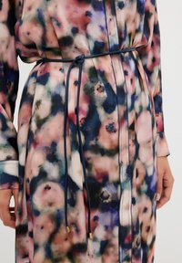 Blommönstrad klänning i mjukt tyg, med bälte i midjan, långa ärmar och en blandning av rosa, blå och gröna färger med en slät yta.