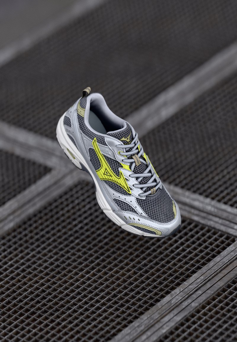 Chaussure de sport grise avec tige en maille, accents jaunes et fermeture à lacets. Semelle texturée, éléments réfléchissants et col rembourré pour le confort.
