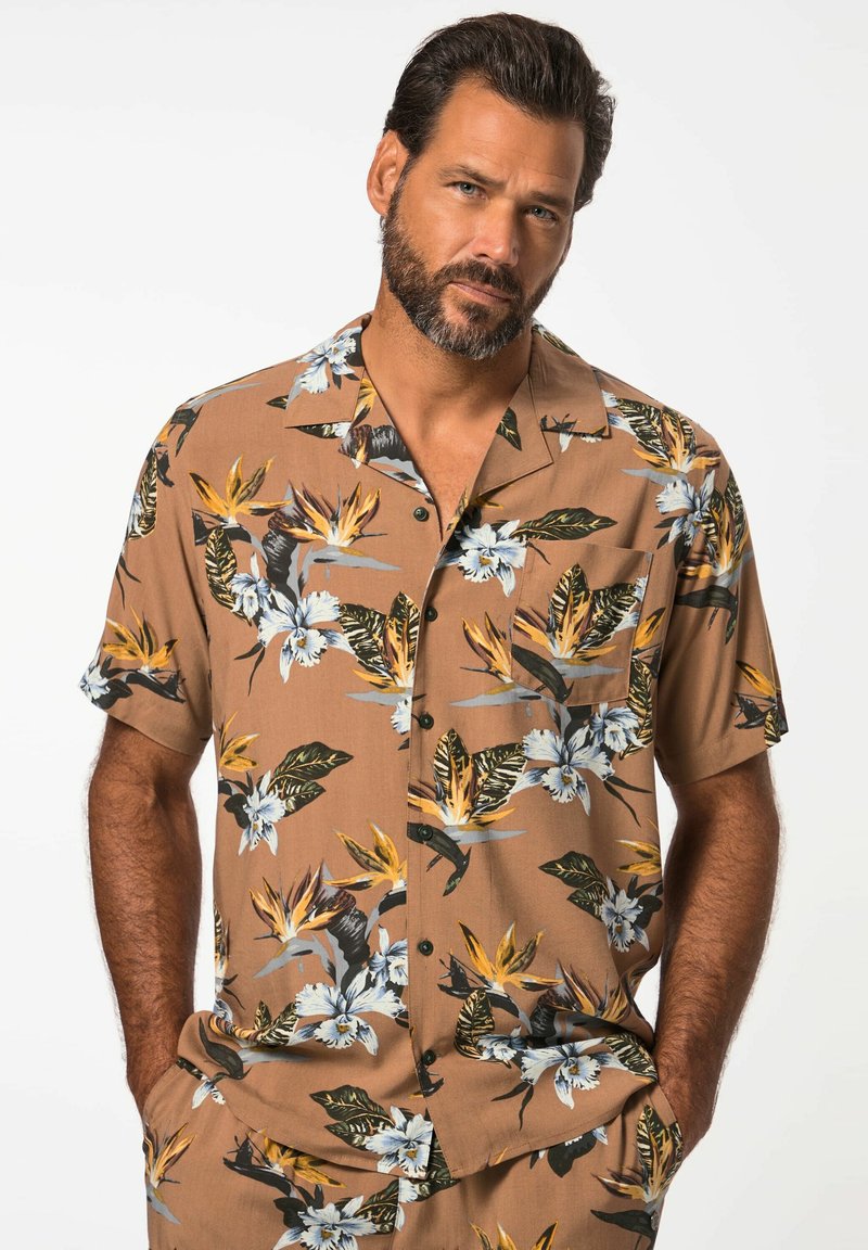 Camisa de manga corta marrón con estampado floral que presenta patrones tropicales con flores blancas y amarillas, hojas verdes y botones negros.