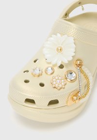 Gold-colored Croc with flower and gemstone accessories, featuring a textured finish, ventilation holes, and a decorative charm.