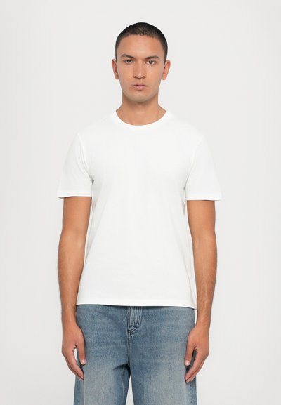 T-shirt en coton blanc à manches courtes, col rond et coupe classique, associé à un jean en denim bleu clair. Design uni, sans motifs.