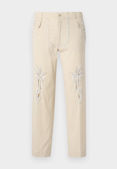 Pantaloni beige in cotone, con un'applicazione intricata di ricami bianchi di piante tropicali sulle gambe e bottoni decorativi sulle tasche.