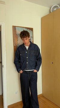 Temno modra denim jakna z dvema žepoma na prsih in zapiranjem na gumbe, v kombinaciji z širokimi jeans hlačami v enaki barvi. Pod njo je enostavna bela majica.