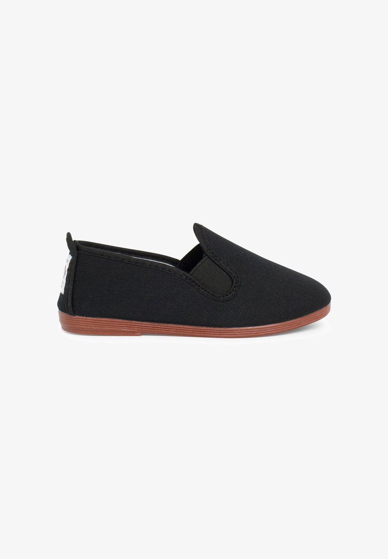 Chaussure noire slip-on avec panneau latéral élastique et semelle plate marron, conçue pour un usage décontracté.