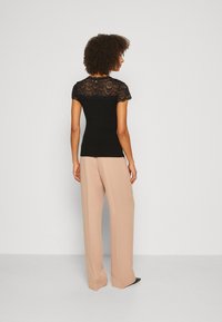 Top negro con mangas cortas de encaje y cuerpo ajustado; combinado con pantalones anchos beige. Tejido suave con un patrón de encaje texturizado en los hombros.