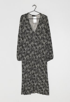 Robe midi noire et blanche à manches longues avec motif à pois dispersés, encolure en V et coupe ample, suspendue à un cintre noir sur fond gris.