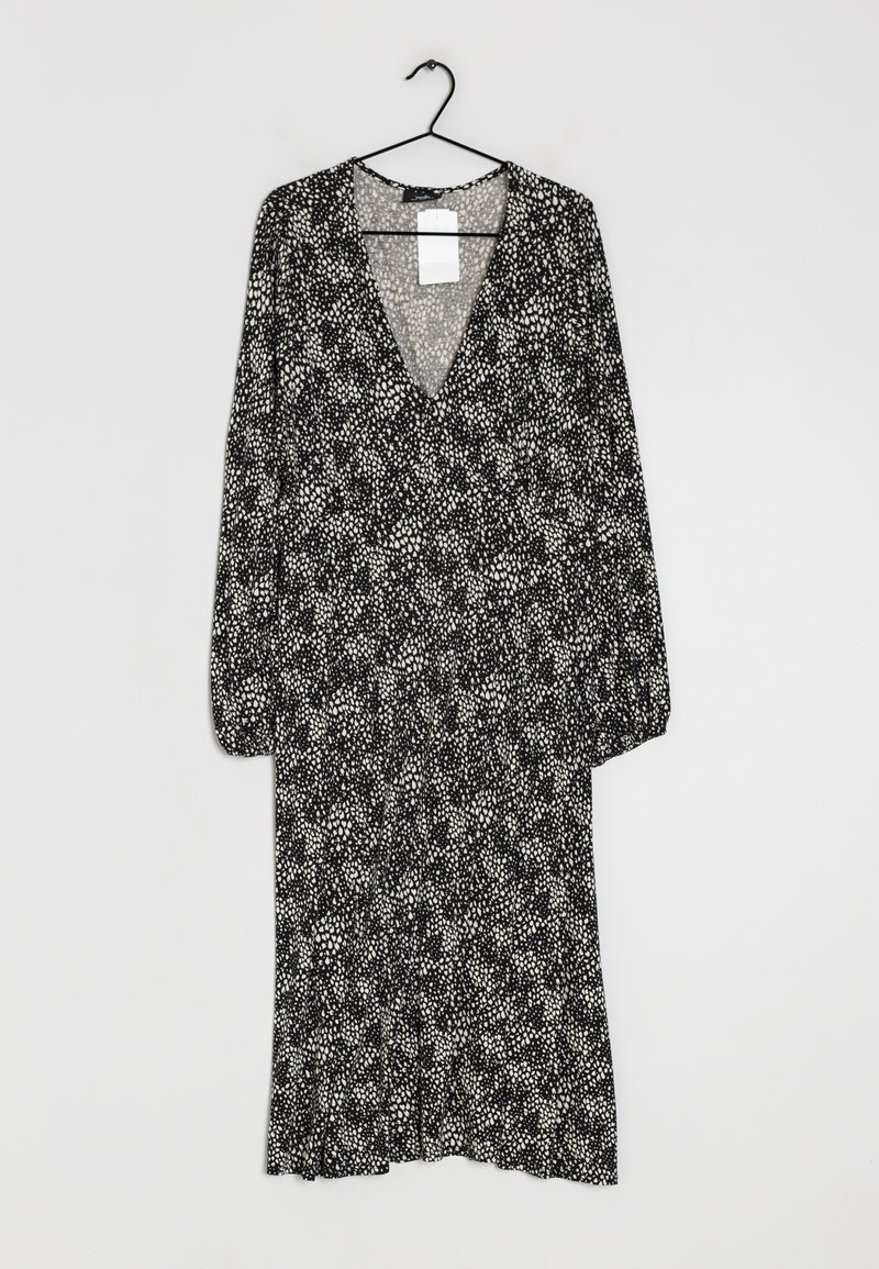 Robe midi noire et blanche à manches longues avec motif à pois dispersés, encolure en V et coupe ample, suspendue à un cintre noir sur fond gris.