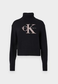 Marineblauwe crop trui met een geribbelde turtleneck, voorzien van een lichtroze geborduurd 'CK' logo en 'calvin klein' tekst. Glad brei-textuur.