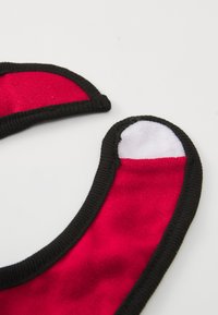 Red fabric bib with black trim and a white accent, featuring rounded edges and a soft texture, designed for easy wear.