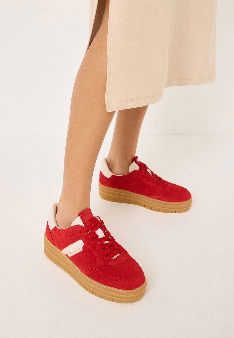 Baskets en suède rouge avec une semelle beige épaisse et des accents blancs. Elles possèdent des lacets ronds et un col rembourré pour le confort.