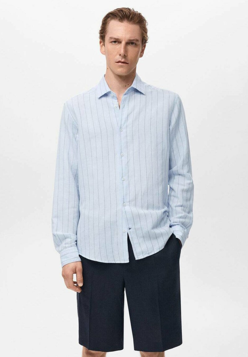 Camisa de botones de rayas azul claro con mangas largas, hecha de una tela suave, combinada con pantalones cortos oscuros. Presenta un cuello clásico y botones frontales.