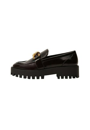 Mocasines de cuero negro con suela gruesa negra, que presentan un destacado adorno de cadena dorada a lo largo del empeine y un acabado liso.