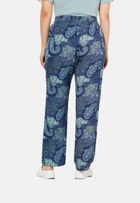Marineblauwe broek met een paisley- en geometrisch patroon in groen en wit. Heeft een relaxte pasvorm en een elastische tailleband, gecombineerd met witte schoenen.