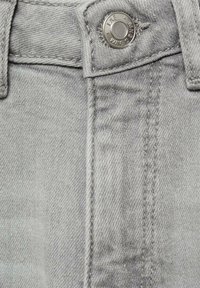 Ljust grå denimtyg med en metallknapp i midjan, synlig sömnad och en slät yta.
