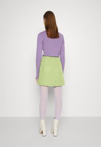 Top roxo de manga longa combinado com uma saia mini verde, collants lilás e botas brancas até ao tornozelo. Tecido suave com uma silhueta ajustada.
