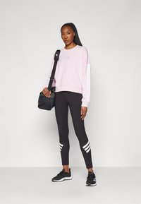Lyse rosa genser med hvite striper på ermene, svarte leggings med tre hvite striper på kanten, og svarte treningssko. Svart veske hengende over skulderen.