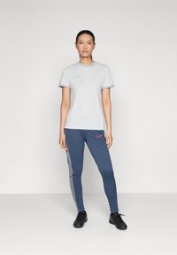 Grå trenings t-skjorte med en turkise Nike-logo, kombinert med blå bukser med røde og grå detaljer og slim fit. Svarte treningssko.