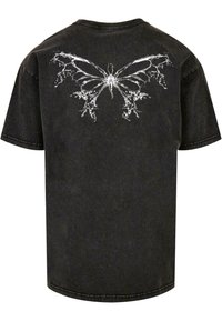 Black cotton t-shirt with a round neck. Features a white butterfly design on the back, accented with abstract patterns and stitching.