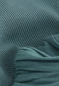 Primo piano di tessuto a maglia coste morbido color verde acqua con aree piegate e testurizzate che creano onde e ombre delicate.