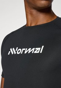 Le t-shirt de sport noir présente un tissu texturé avec une coupe ajustée. Un texte blanc en grande taille indique "Normal" sur la poitrine.