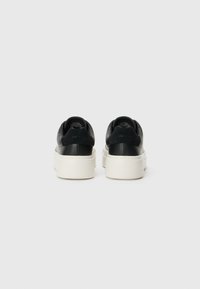 Baskets plateformes en cuir noir avec une épaisse semelle blanche. Texture lisse avec un logo subtile sur le talon et un design arrondi à l'arrière.