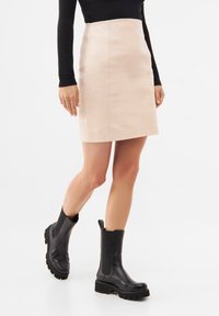 Kožená mini sukně v světle béžové barvě, s přiléhavým střihem. V kombinaci s černými mohutnými kotníkovými botami a dlouhým černým topem.