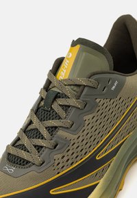 Olivgrüner Mesh- und synthetischer Sportschuh mit gelben Akzenten, verstärkter Zehenkappe und strukturiertem Sohlendesign. Verfügt über einen gepolsterten Kragen und ein Schnürsystem.