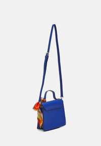 Blå läder crossbody-väska med ett handtag, rektangulär form, guldfärgad hårdvara och en färgglad silkscarf knuten på ena sidan.