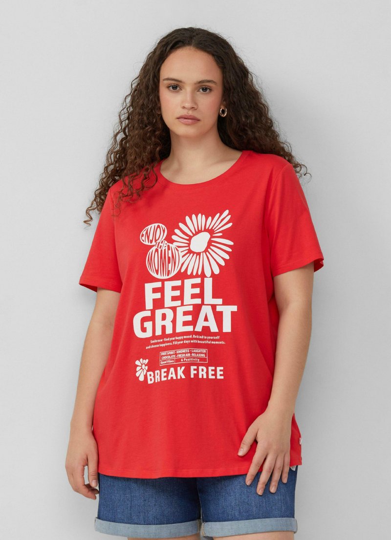 Czerwona bawełniana koszulka z krótkim rękawem, z białym napisem i grafiką kwiatową. Dół jest prosty, a koszulka zestawiona jest z dżinsowymi szortami.