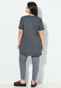 Tunique grise à manches courtes avec un ourlet arrondi, associée à un pantalon gris. L'ensemble présente une coupe décontractée, avec des chaussures slip-on à imprimé animal.