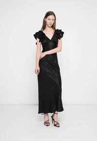 Melna midi kleita no faktūrēta auduma ar volāniem piedurknēs un V veida izgriezumu. Siluets ir piegulošs ar vieglu paplašinājumu apakšā.