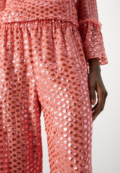 Pink fabric outfit adorned with small, shiny sequins in various shades, featuring a textured pattern and elastic waistband.
