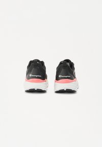 Zwarte sportieve schoenen met een gestructureerde mesh bovenkant, roze en gele accenten, trek-lussen bij de hiel, en een witte geprofileerde zool.