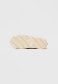 Κρέμα από καουτσούκ σόλα παπουτσιών που διαθέτει υφή με ραβδωτό σχέδιο και κεντρικό λογότυπο σε ορθογώνιο σχήμα. Συμπαγές, στρογγυλό σχήμα δαχτύλων.