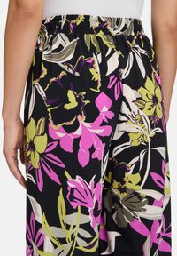 Kwiatowe spodnie szerokie nogawki z elastycznym paskiem w talii, z czarnym tłem, dużymi różowymi, zielonymi i białymi wzorami kwiatowymi oraz gładką fakturą materiału.