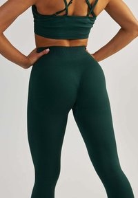 Des leggings de sport vert foncé présentent une taille haute avec une texture côtelée. Le design inclut un aspect sans couture et des accents de contour à l'arrière.