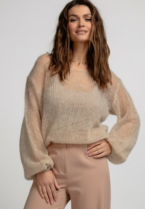 Beżowy, dziany sweter o luźnym kroju, z balonowymi rękawami i szerokim dekoltem. Miękki, teksturowany materiał tworzy przezroczysty wygląd.