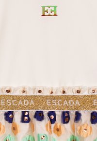 Top in tessuto bianco con applicazioni floreali multicolori e una fascia dorata lucida con la scritta "ESCADA" in lettere bianche sul fondo.