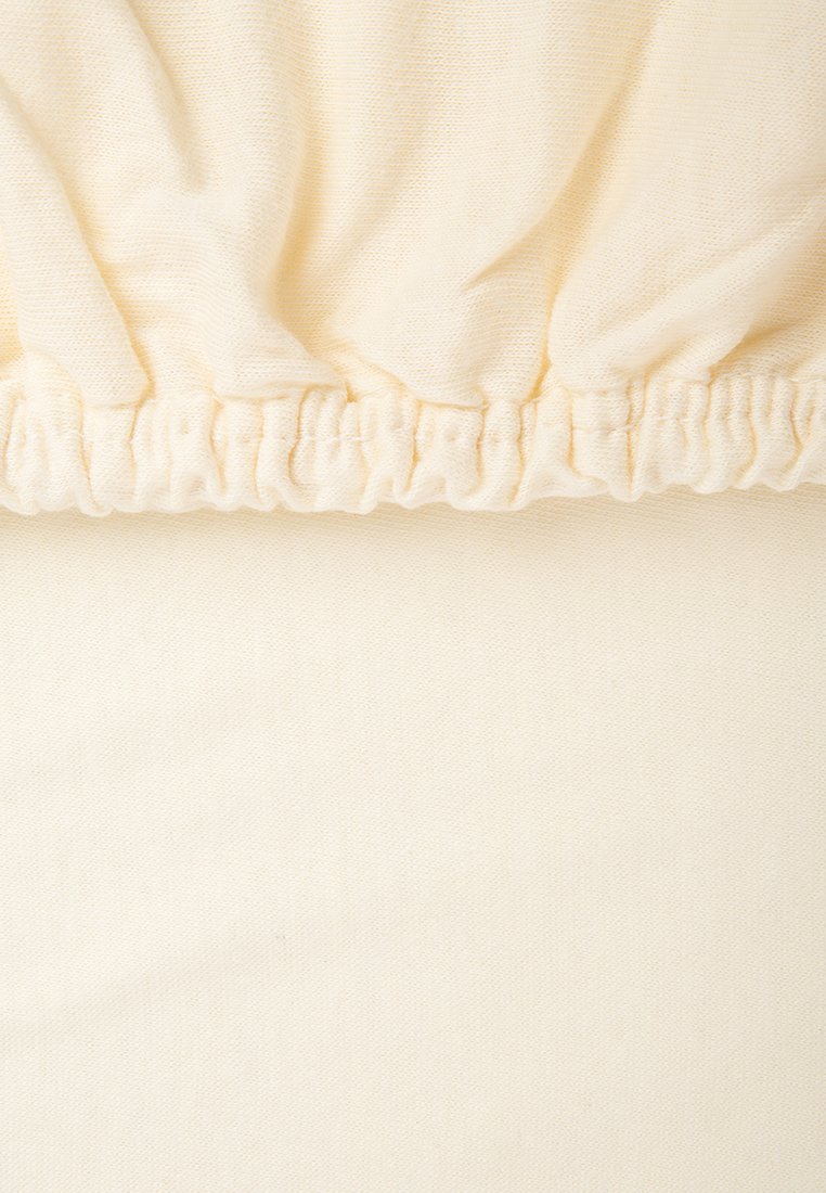 Baumwoll-Spannbettlaken in sanftem Cremeton mit elastischen Kanten, das eine glatte Textur und ein dezentes, dicht gewebtes Stoffmuster aufweist.