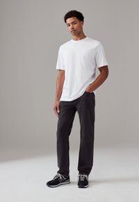 Fehér rövid ujjú póló, sötétszürke, egyenes szabású farmernadrággal, fekete, fehér és szürke részletekkel díszített tornacipővel párosítva. Egyszerű dizájn, kényelmes, hétköznapi fazon.