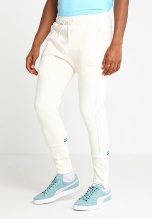 Osoba nosząca kremowe spodnie dresowe Puma z wiązaniem w pasie oraz jasnoniebieskie sneakersy Puma z białymi podeszwami i dodatkami.