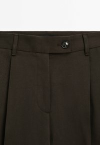 Pantalon marron foncé taillé sur mesure avec passants pour ceinture et fermeture à bouton noir à la taille, présenté sur fond blanc.