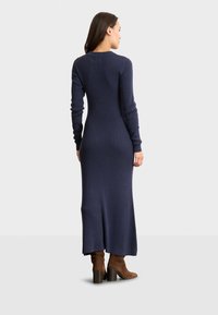 Abito in maglia a coste blu navy con maniche lunghe, scollo a giro e un taglio lungo e dritto. Indossato con stivali alla caviglia in suede marrone e una leggera apertura posteriore.