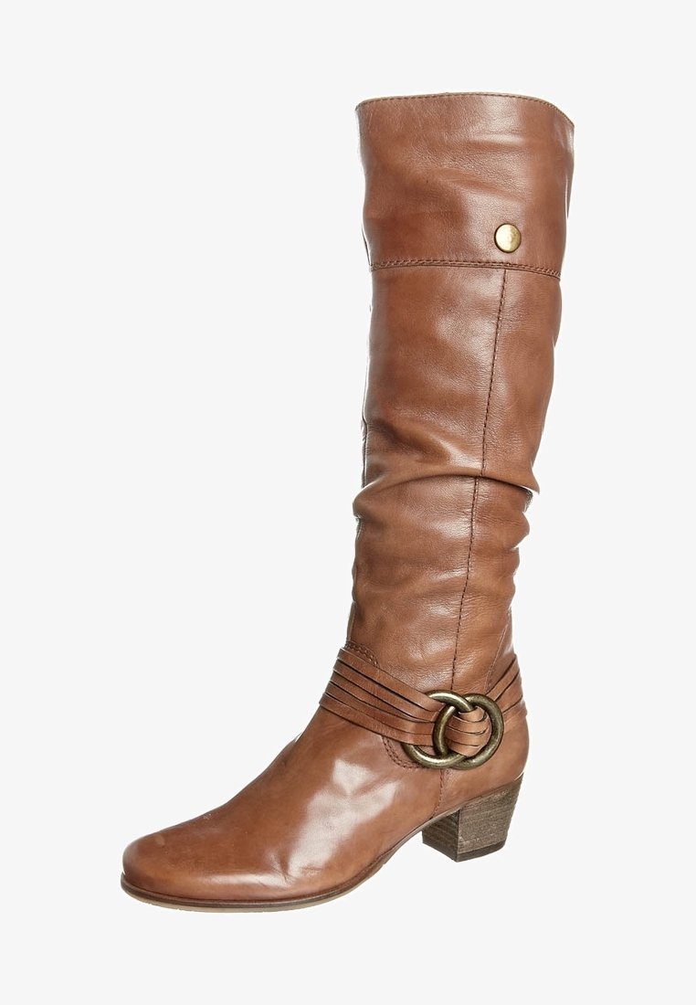Botte haute en cuir marron jusqu'au genou avec talon bas empilé, sangle décorative et détail en anneau métallique sur le côté extérieur.