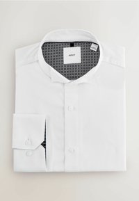 Balta marškiniai, pagaminti iš tekstūruoto audinio, su sagomis priekyje, standartiniu apykakle ir kontrastingomis raštuotomis vidinėmis detalėmis.
