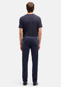 Pantaloni chino blu navy a vestibilità slim, realizzati in tessuto misto cotone. Vista posteriore con due tasche e dettagli di cuciture sottili. Abbinati a una maglietta basica.