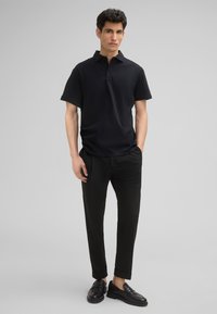 Czarna koszulka polo z krótkim rękawem, z kołnierzykiem i trzema guzikami. Noszona z czarnymi spodniami i mokasynami.